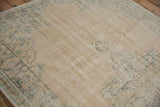 Rectangular vintage Oushak carpet in muted beige with soft green floral and medallion patterns, showing a distressed, worn texture on wooden floor.