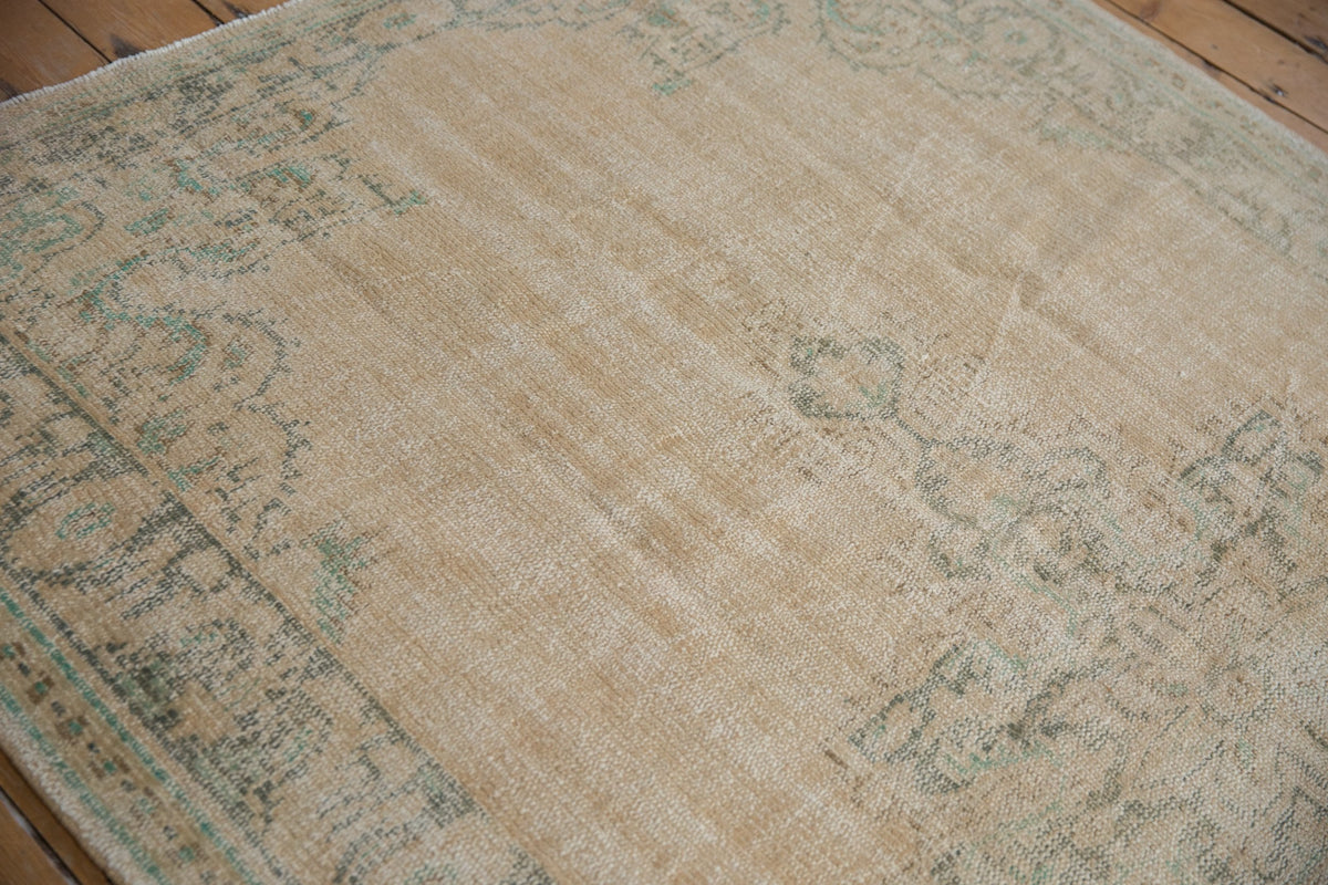 Rectangular vintage Oushak carpet in muted beige with soft green floral and medallion patterns, showing a distressed, worn texture on wooden floor.