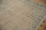 Faded beige and light green vintage Oushak carpet with distressed patterns on a hardwood floor, showing subtle worn floral and geometric motifs.