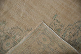 Close-up of a vintage distressed Oushak carpet in beige tones with faded blue and grey floral patterns, showing the carpet's texture and folded corner.