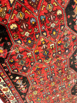 Close-up of a vintage Persian Hosseinabad runner rug with a red field, geometric medallions, and intricate multicolored tribal motifs framed by a dark border.