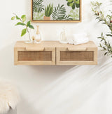 Light wood floating console with two rattan-front drawers, decorated with glass vases and white rolled towels, set against a white wall with botanical artwork above.