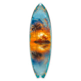 Surfboard-shaped wall art depicting a tropical island with palm trees reflected on calm water under a vibrant orange and blue sunset sky.
