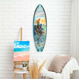 Surfboard-shaped wall art featuring a mermaid with flowing golden hair sitting on rocks at sunset with ocean reflections, mounted on a white brick wall above a beige couch.