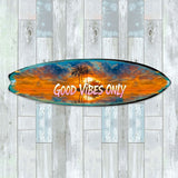 Surfboard-shaped wall art featuring a vibrant tropical sunset with palm trees and the phrase 'GOOD VIBES ONLY' in pink and white lettering across the center.
