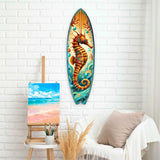 Surfboard-shaped wooden wall art featuring a detailed brown seahorse with turquoise ocean waves and bubbles on a sandy background, displayed on white brick wall.