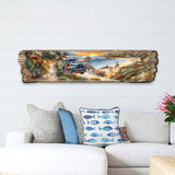 Long wooden wall art depicting a coastal sunrise with a vintage blue truck on a sandy path, colorful bushes, and waves crashing on rocky shores under an orange sky.
