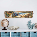 Long wooden plaque with a painted coastal scene showing a blue vintage truck on a beachside path, rocky shore, ocean waves, and a sunset sky, hung above blue baskets.