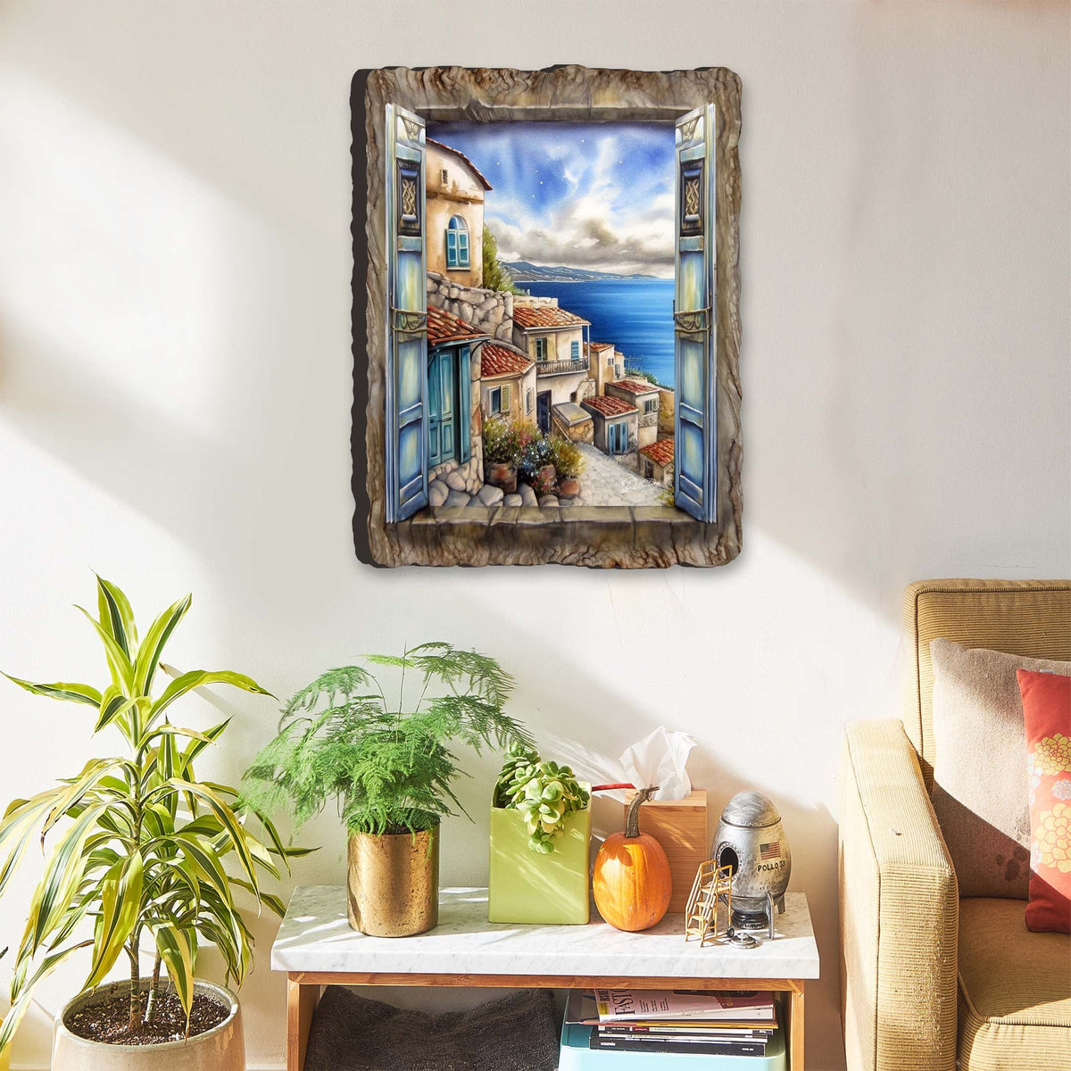 Wall art showing an open blue window with shutters framing a sunny Mediterranean coastal townscape, stone buildings, blue sky, and sea beyond, in a rustic wood frame.