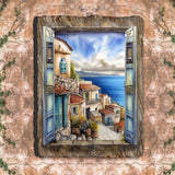 Painted window with blue shutters opens to a coastal village scene featuring terracotta rooftops, stone steps, and a calm blue sea under a partly cloudy sky.
