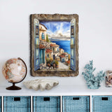 Wall art showing a coastal town viewed through open blue shutters with stone buildings and blue ocean under a bright sky, framed by a textured rustic border.
