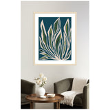 Framed abstract botanical print with pink and green leaves outlined in white against a deep blue background, hanging above dark green velvet armchairs and wooden round table.
