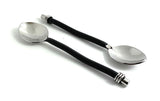 Two teaspoons with shiny silver bowls and black curved handles featuring silver accents at both ends, arranged on a white background.