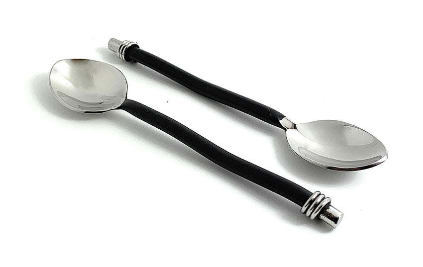 Two teaspoons with shiny silver bowls and black curved handles featuring silver accents at both ends, arranged on a white background.
