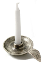Silver metal taper candlestick holder with a textured round dish and an attached leaf-shaped handle, holding a white taper candle upright.