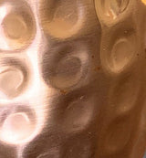 Close-up of a hammered texture on a metallic surface featuring irregular circular indentations with a warm copper tone and reflective highlights.