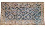 Rectangular vintage distressed Soumac carpet with beige background, blue geometric medallions, and muted brown and rust accents in intricate patterns.