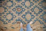 Vintage distressed Soumac carpet with faded teal background and geometric floral patterns in beige, pink, and brown tones, viewed from above with feet at bottom edge.
