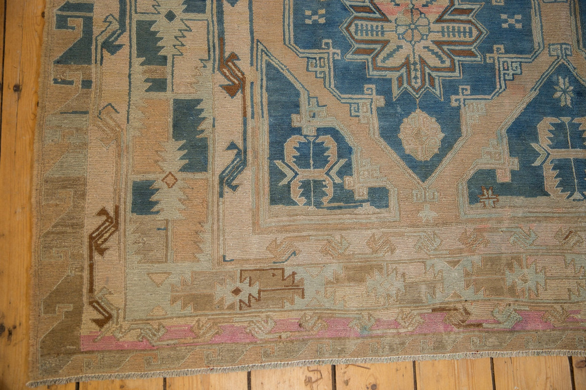 Vintage Soumac carpet corner with distressed faded blue, beige, and brown geometric patterns and a thin pink border on hardwood flooring.