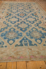 Vintage distressed Soumac rug with blue geometric star and floral patterns on beige background, lying on wooden floorboards, showing soft faded colors and worn edges.