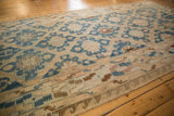 Vintage distressed Soumac carpet with cream, blue, and tan geometric floral patterns laid on honey-colored wooden floorboards.