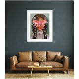 Framed portrait of a woman with braided hair adorned with flowers, wearing a vintage lace blouse, and large pink moths covering her eyes, hung on a dark teal wall above a brown leather sofa.