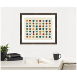 Framed abstract art print featuring seven rows of colorful dots in earthy tones on a cream background, hung above a desk with books, plant, and mug.