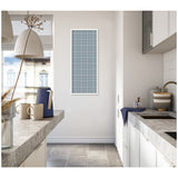 Tall kitchen with light gray concrete countertops and white cabinets, featuring a vertical blue plaid framed fabric pinboard centered on the far wall.