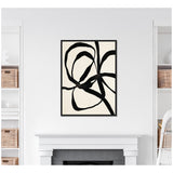Abstract black twisted ribbons on a cream background in a black rectangular frame, hung above a white mantel in a minimalistic room with white shelves and wicker baskets.