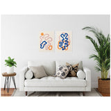 Two framed abstract line art prints with beige backgrounds and blue, orange, and pink curving shapes hanging above a white sofa with mixed-pattern pillows in a minimalist living room.