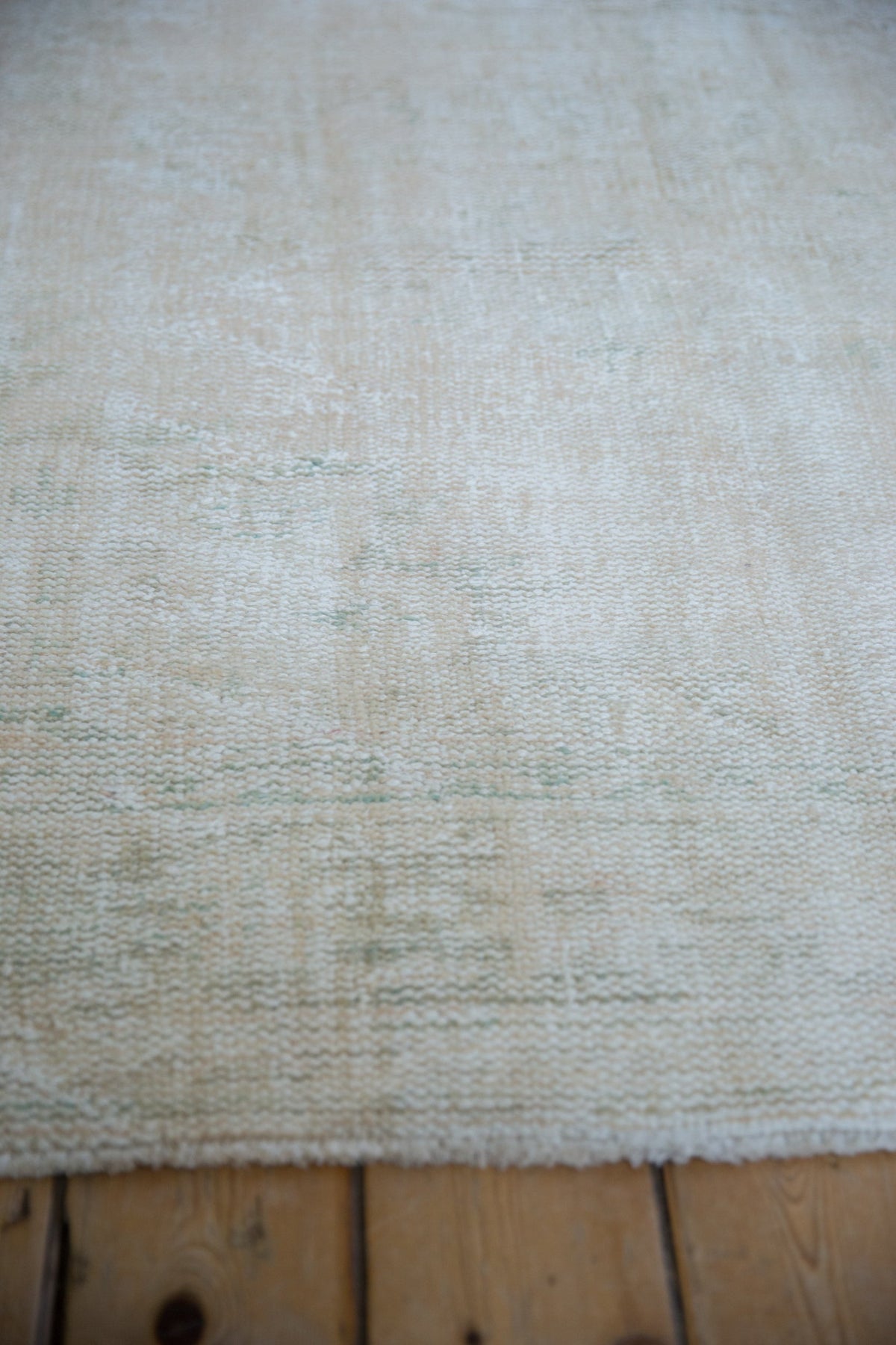 Close-up view of a 5x8.5 vintage distressed Oushak carpet with soft beige tones and subtle textured patterns on a wooden floor.