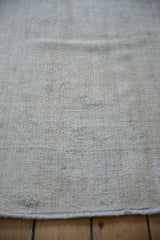 Close-up view of a vintage distressed Oushak carpet in muted beige and cream tones with subtle hints of blue and worn texture.