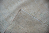 Close-up of a vintage distressed Oushak carpet in muted beige and pale blue tones with a coarse, textured weave.