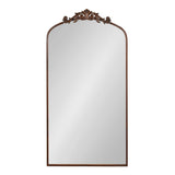 Tall rectangular mirror with an arched top and dark brown ornate carved floral crest along the upper edge, set against a plain white background.
