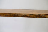 Close-up side view of a honey-toned wooden table top edge showcasing natural wood texture and grain against a plain light background