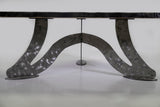 Curved metallic base with a brushed, hammered texture supporting a dark tabletop, shown from a low side angle against a plain background.