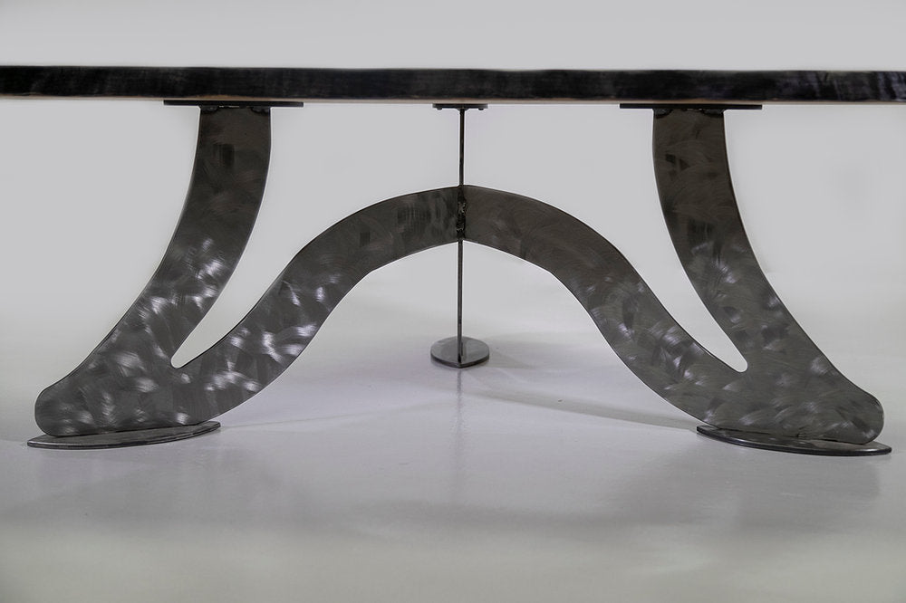 Curved metallic base with a brushed, hammered texture supporting a dark tabletop, shown from a low side angle against a plain background.