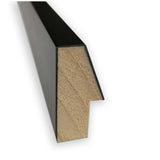Close-up of a rectangular wooden molding piece with a black painted outer surface and a stepped, light natural wood inner profile.