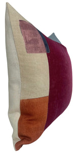 Rectangular pillow cover with color-blocked panels in claret red, beige, rusty orange, and a small navy blue accent, shown from a side angle.
