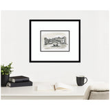 Black and white framed watercolor painting of a Venice canal with gondolas and historic buildings, hung on a white wall above a desk with books, an open notebook, a black mug, and a plant.