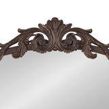 Close-up of the top center of an arched mirror frame with ornate dark brown scrollwork and leaf motifs against a light background.