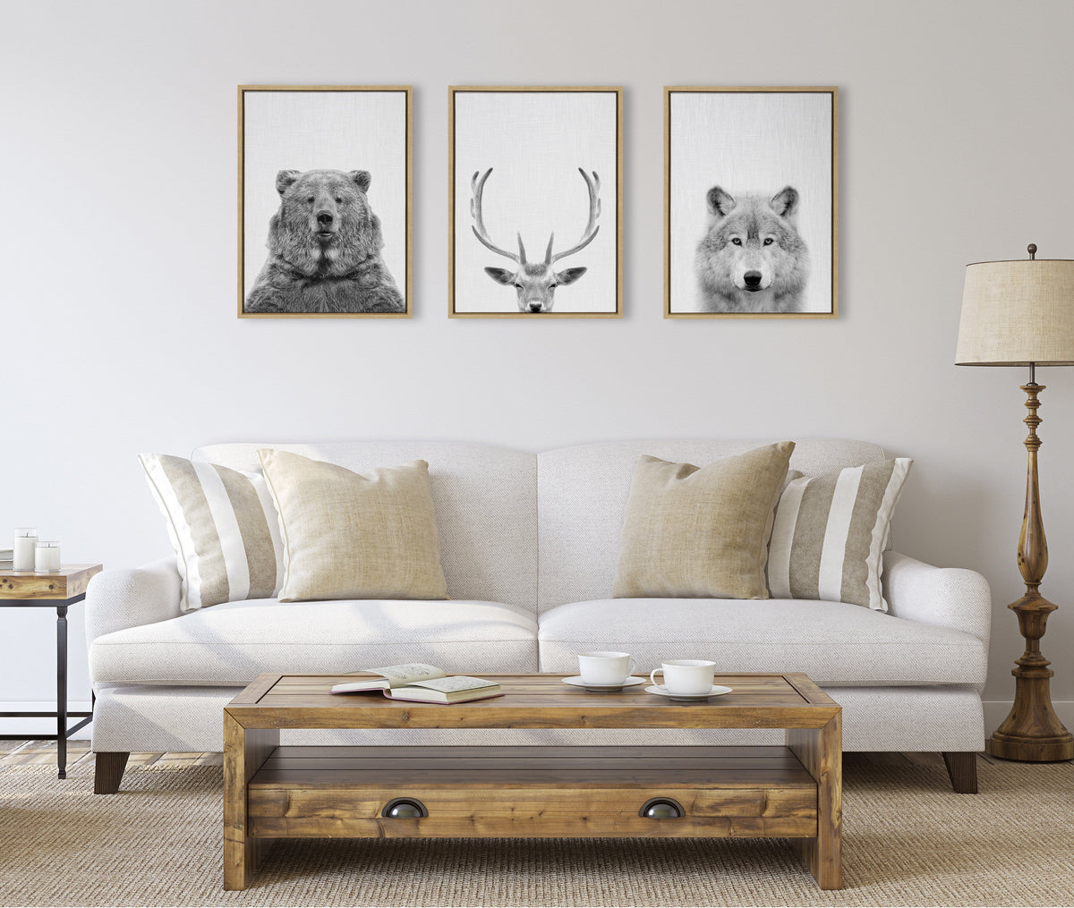 Three framed black and white animal portraits—a bear, a deer with large antlers, and a wolf—hanging above a beige sofa with neutral pillows in a minimalist living room.