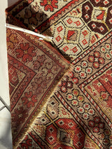 Close-up of an antique Turkish wool prayer rug with worn patterns in red, beige, and brown featuring geometric and floral motifs and frayed edges.