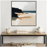 Abstract coastal landscape painting with beige sandy shore, dark rocky cliffs, and blue-gray ocean under a pale sky, framed and hung above a wooden table with decor.