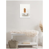 Framed canvas art of a curly golden doodle dog sitting in a white clawfoot bathtub with a towel draped over the side, displayed on a light gray wall above a white bench with a fur throw.
