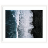 Aerial view of ocean waves crashing against a black pebble beach with white foamy patterns, framed in white narrow moulding