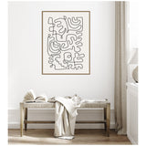 Black abstract continuous line art on white canvas in a thin wood frame, hanging above a rustic wooden bench with an open book and light beige fabric.