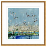 Painting of mallard ducks flying over reeds with several ducks resting near a body of water under a pale blue sky, framed in gold.
