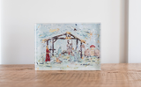 Small acrylic tabletop artwork depicting a Nativity scene with Mary, Joseph, baby Jesus, and the Star of Bethlehem in soft pastel colors, placed on a wooden surface.
