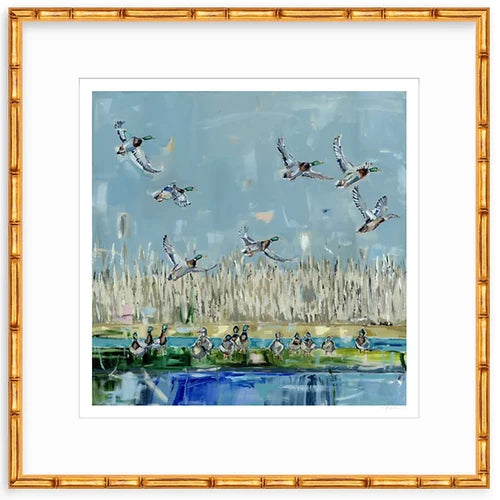 Art print showing mallard ducks flying above a marsh with tall reeds and water reflecting blues and greens, framed in gold bamboo-like frame.